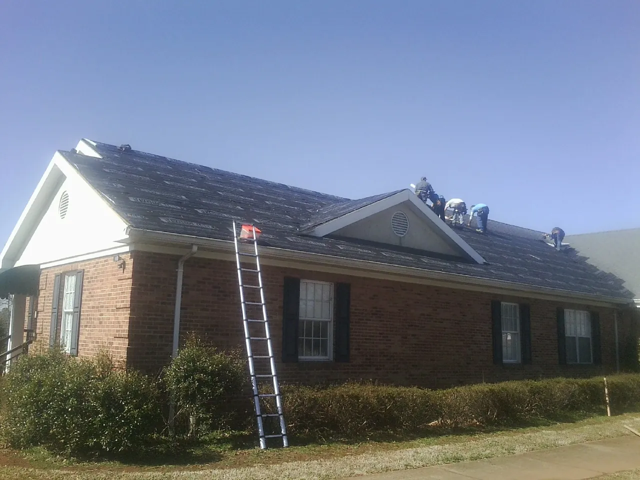 Crew tearing shingles off a brick ranch roof with a ladder set — Emergency Roof Repair work by our crew in Smock