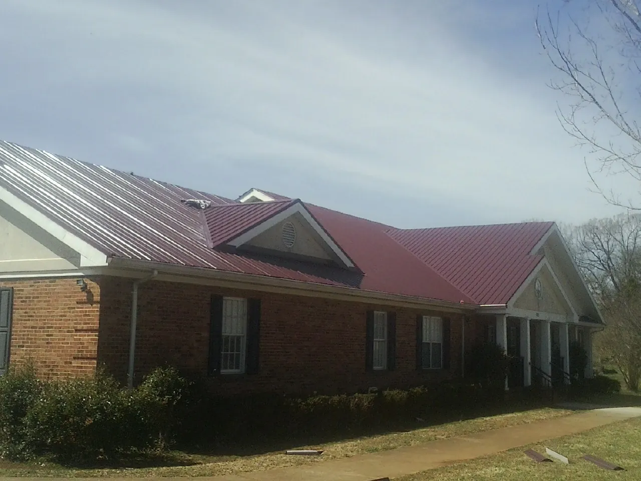 Red metal roof with gabled entries on a long brick building, from a Hail Damage Roof Repair job in Smock