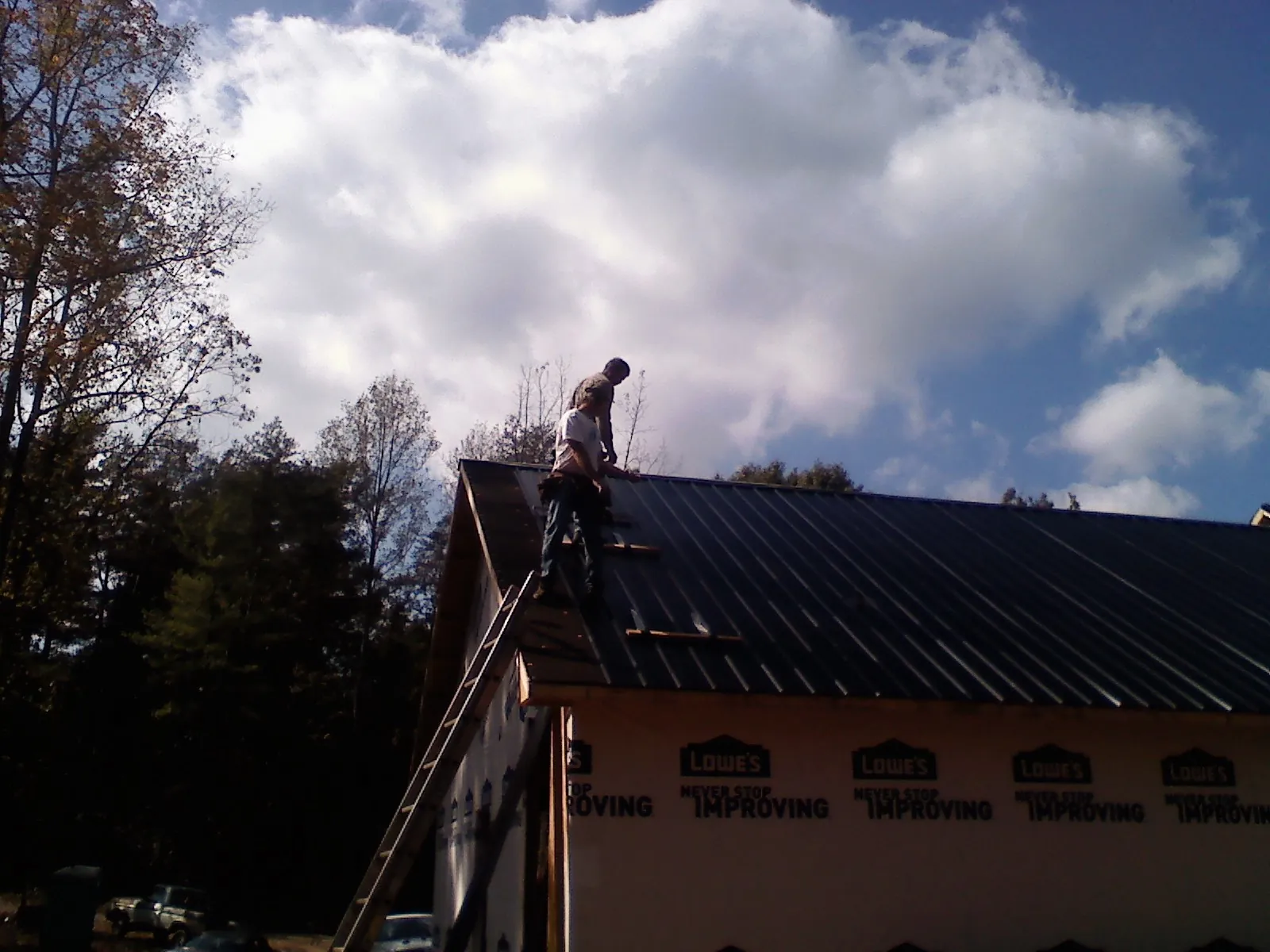 Roofer fastening dark metal panels high against a cloudy sky, from a Roof Inspection job in Smock