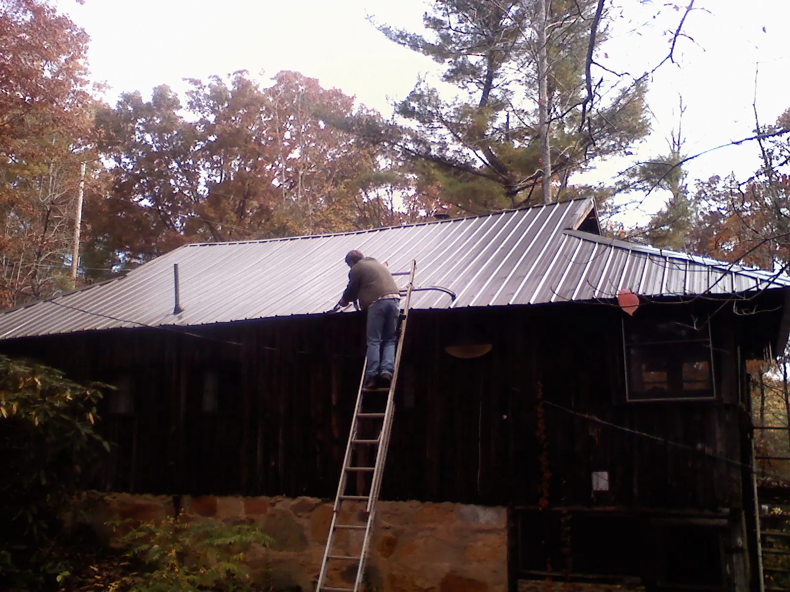 Roofer on a ladder working along the edge of a cabin metal roof in Smock